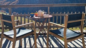Eine Holzterrasse mit Stühlen und einem Tisch, mit Blick auf eine gebirgige Landschaft.