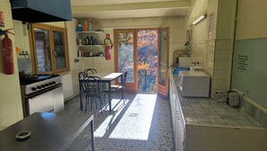Eine Küche mit Gasherd, Spüle und einem Essbereich mit Stühlen. Ein Fenster bietet Blick auf Bäume.