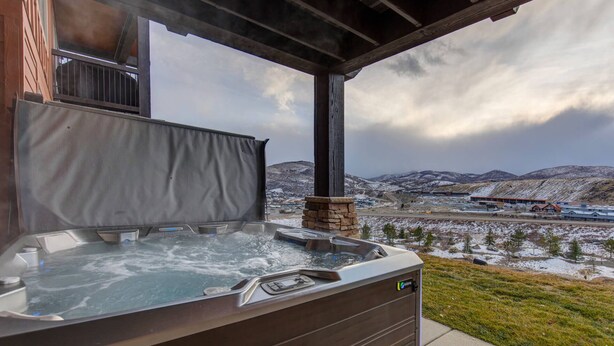 A hot tub with a stone base, set against a backdrop of snow-covered hills and a cloudy sky. - Moose Mgmt at Black Rock 14151: Hot Tub, Views, Grill, King Beds (Park City)