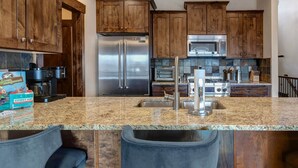A modern kitchen with wooden cabinets, stainless steel appliances, granite countertops, and a bar area with stools. - Moose Mgmt at Black Rock 14151: Hot Tub, Views, Grill, King Beds (Park City)