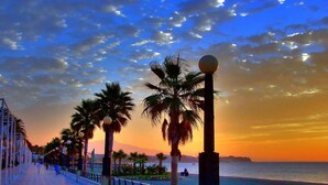 A seaside promenade with palm trees and a sunset. - Seaside Stay With Pool (Estepona)