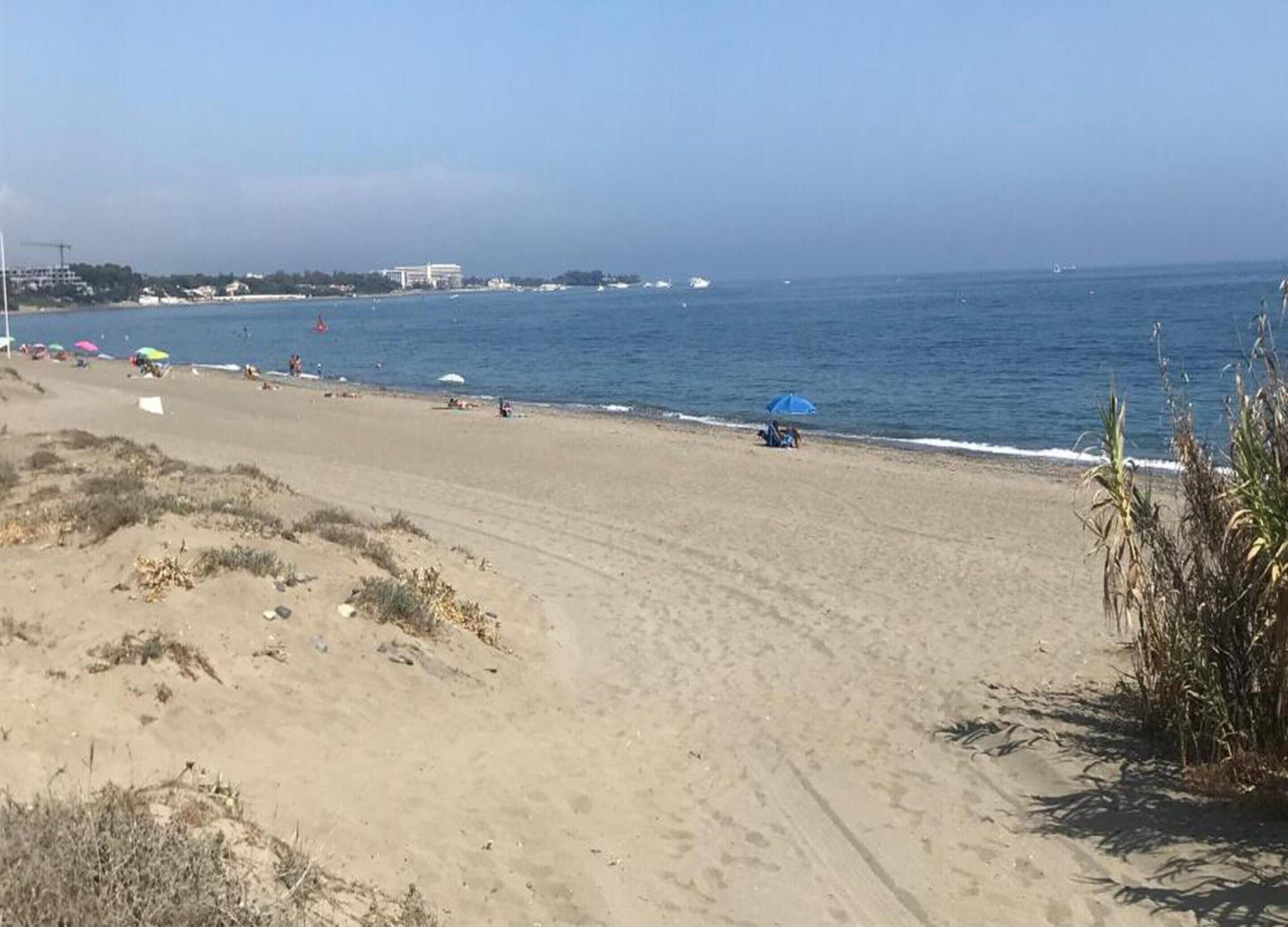 A beach with a sandy shore, a few umbrellas, and a clear view of the ocean.