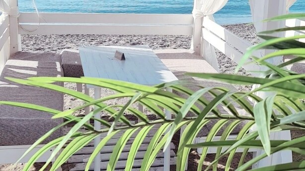 A beachside lounge with a view of the sea, a hanging light fixture, and a white canopy. - Seaside Stay With Pool (Estepona)