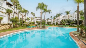 A swimming pool surrounded by palm trees and lounge chairs, with a building in the background. - Seaside Stay With Pool (Estepona)