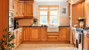 Een keuken met houten kastjes, een fornuis, een spoelbak en een raam met zonwering.
