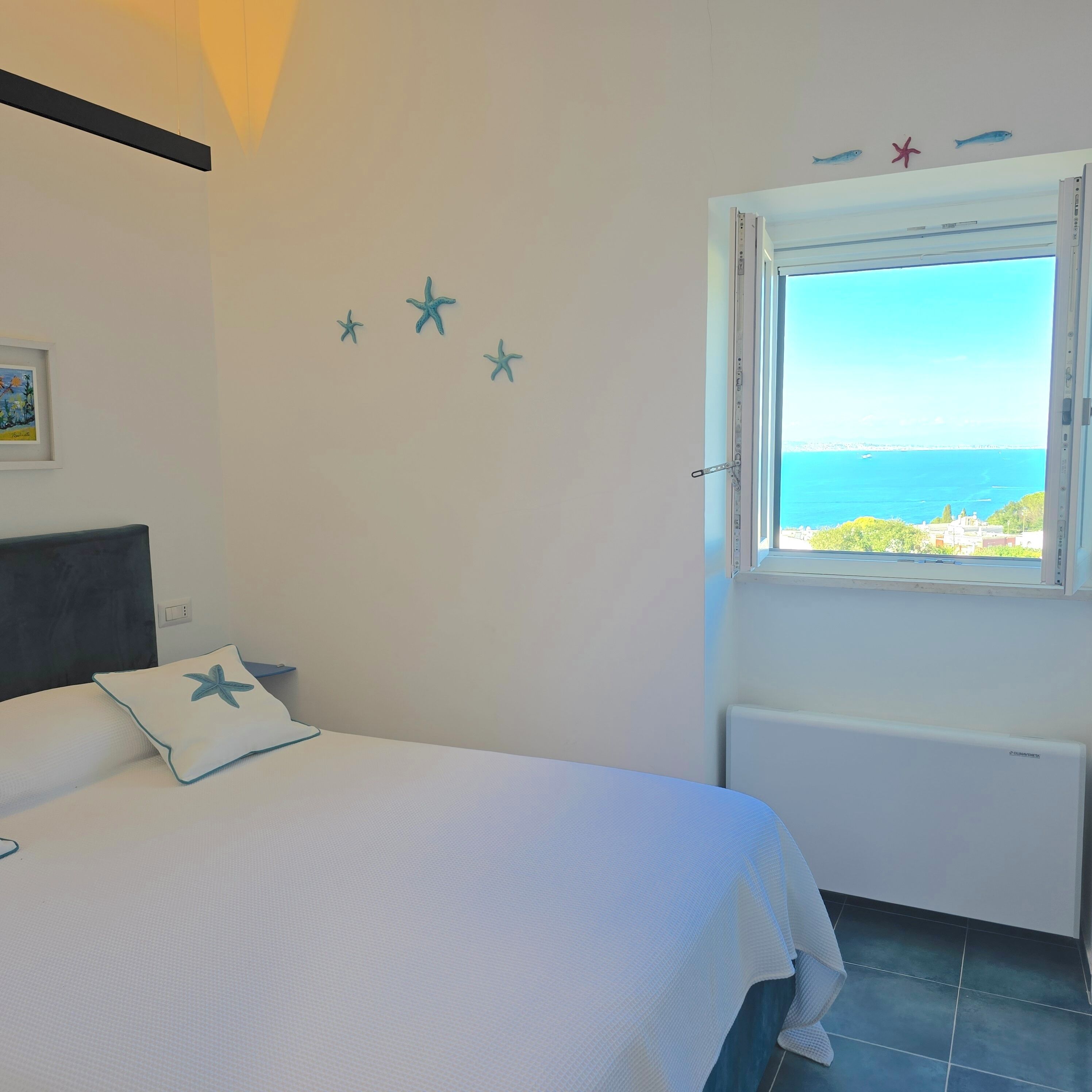 Ein Schlafzimmer mit Bett, einem Fenster mit Meerblick und Wanddekorationen mit Meeressternen.