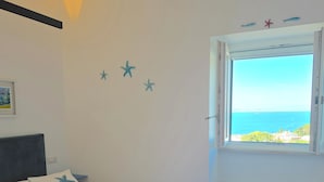 A bedroom with a bed, a window with a view of the sea, and starfish decorations on the wall.