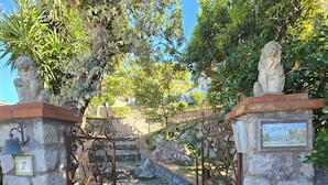 A stone gate with intricate metalwork, leading to a stone staircase surrounded by lush greenery.