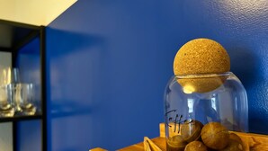 Un frasco de vidrio con tapa de corcho que contiene varios objetos redondos, sobre una superficie de madera frente a una pared azul.