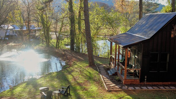A lakeside cabin with a deck, a table and chairs, and a view of the lake and surrounding trees. - Hidden Springs Cottage, Rome, GA, King Loft Bedroom, Private Lake Access (Rome)