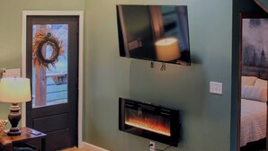 A room with a fireplace, a television mounted on the wall, and a staircase leading to an upper level. - Hidden Springs Cottage, Rome, GA, King Loft Bedroom, Private Lake Access (Rome)