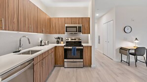 A modern kitchen with wooden cabinets, stainless steel appliances, and a small dining area with a table and chairs. - Exceptional 2BR ! Free Parking ! 30 Min to NYC ! (Newark)