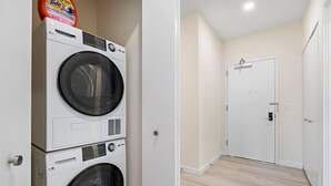 A laundry area with stacked washing machines and a door leading to a hallway with wooden flooring. - Exceptional 2BR ! Free Parking ! 30 Min to NYC ! (Newark)