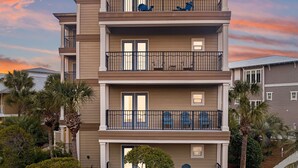 A multi-story residential building with balconies, a small garden, and palm trees.