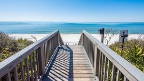 A wooden boardwalk leading to a beach with clear blue water and a clear sky.