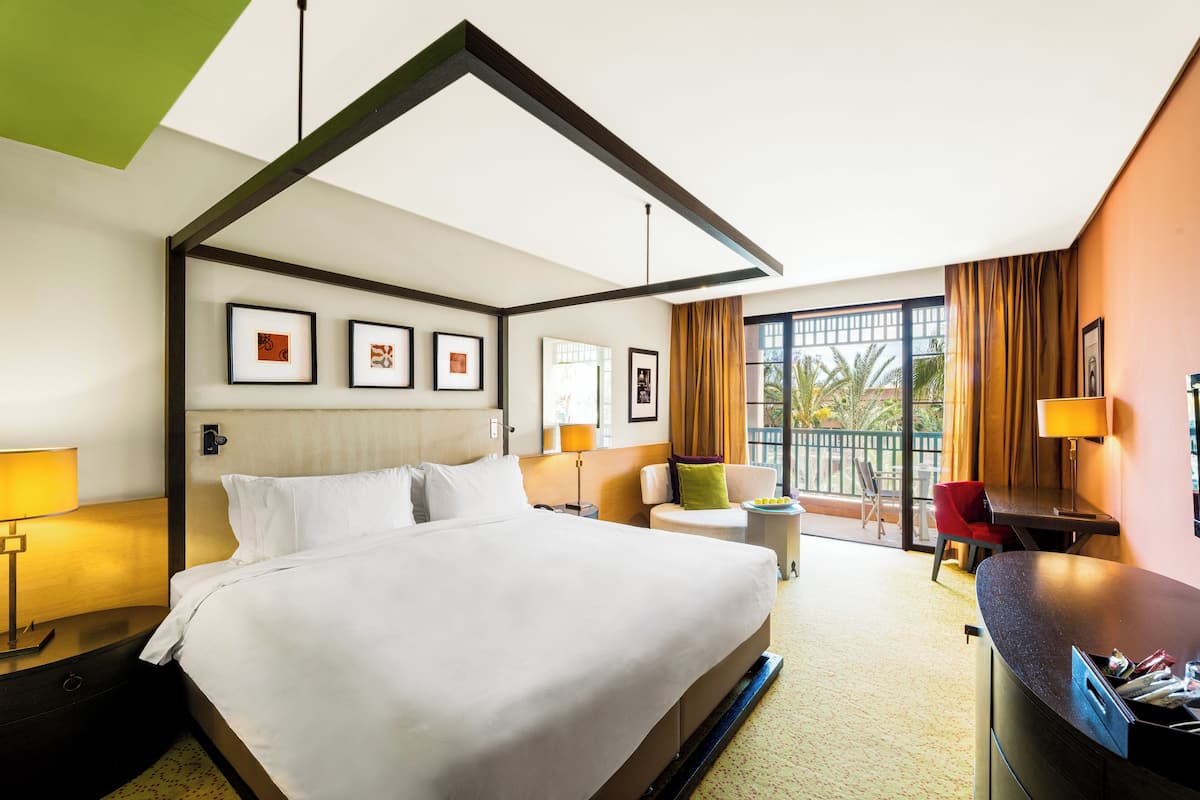 Une chambre d’hôtel avec un grand lit, un bureau, une chaise, une petite table avec une lampe et une vue sur l’extérieur.