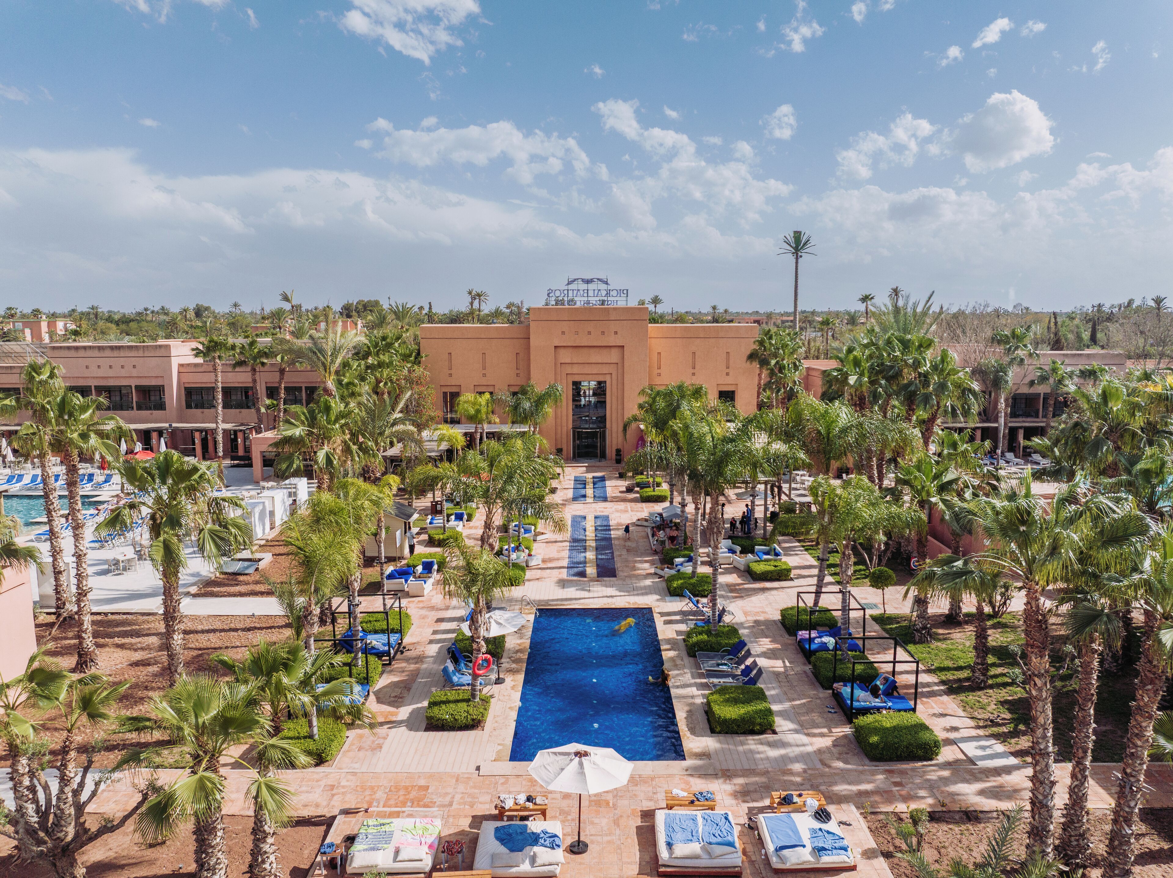 Ein Resort mit einem zentral gelegenen Schwimmbad, Palmen und Liegebereichen.