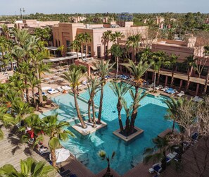 A resort with a central swimming pool surrounded by palm trees, lounge chairs, and a poolside deck. - Pickalbatros Hôtel Du Golf - Adults Friendly 16 Years Plus- All-Inclusive (Marrakech)
