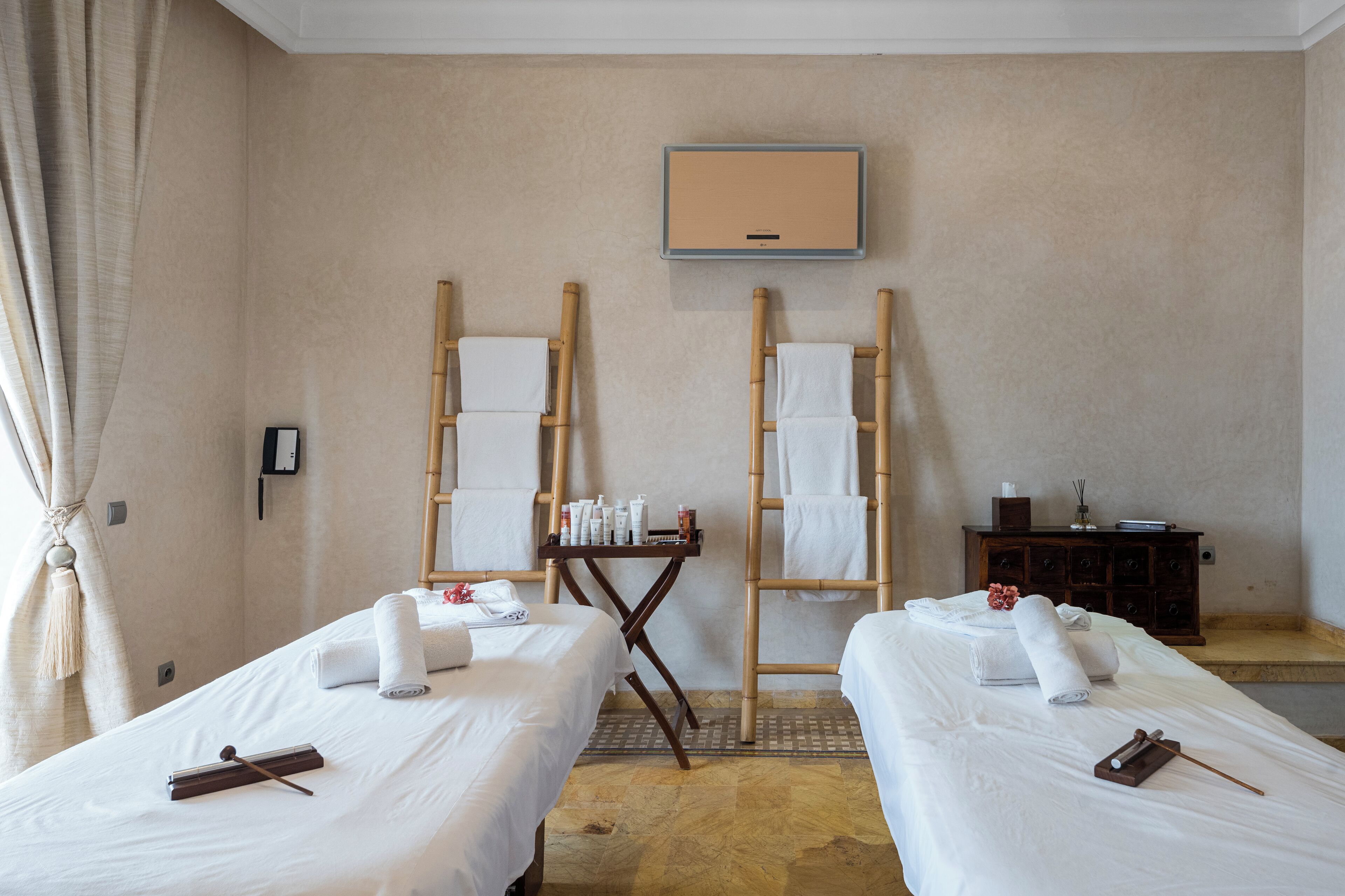 A hotel room with two beds, a small table with toiletries, a mirror, and a TV mounted on the wall.