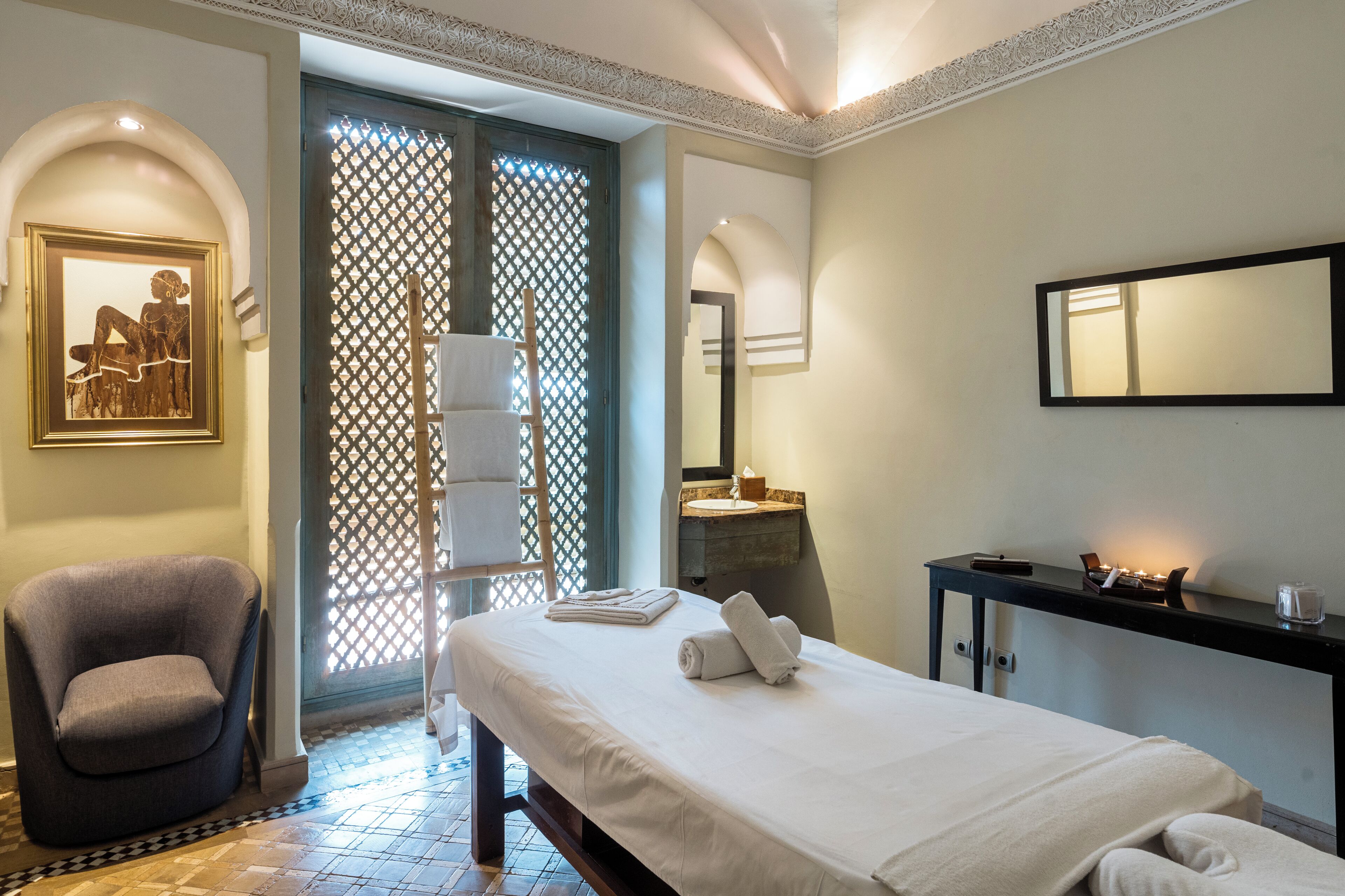Una habitación de hotel con una cama, una silla, un baño con lavamanos y un espejo.