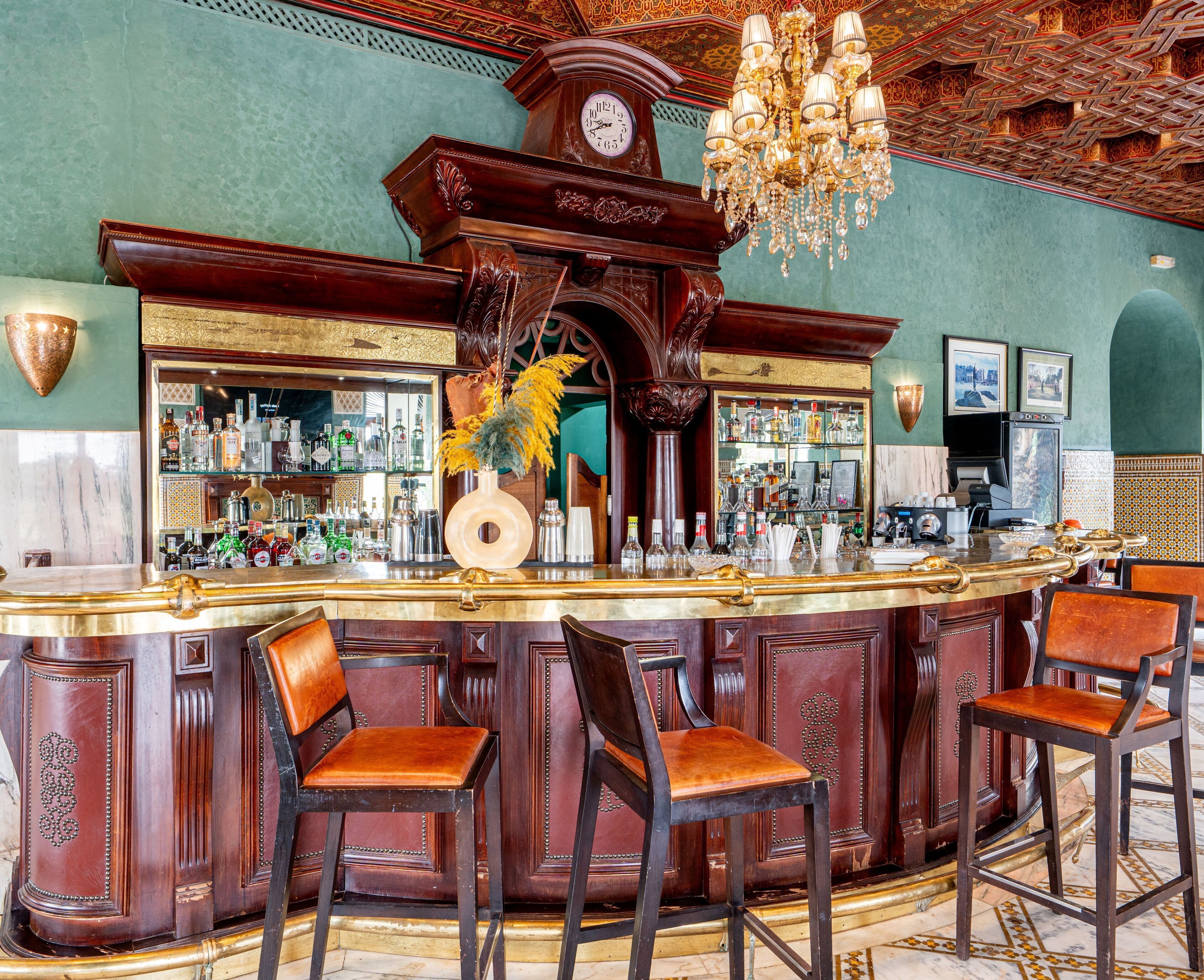 A bar area with a wooden counter, bar stools, a clock, and a chandelier.