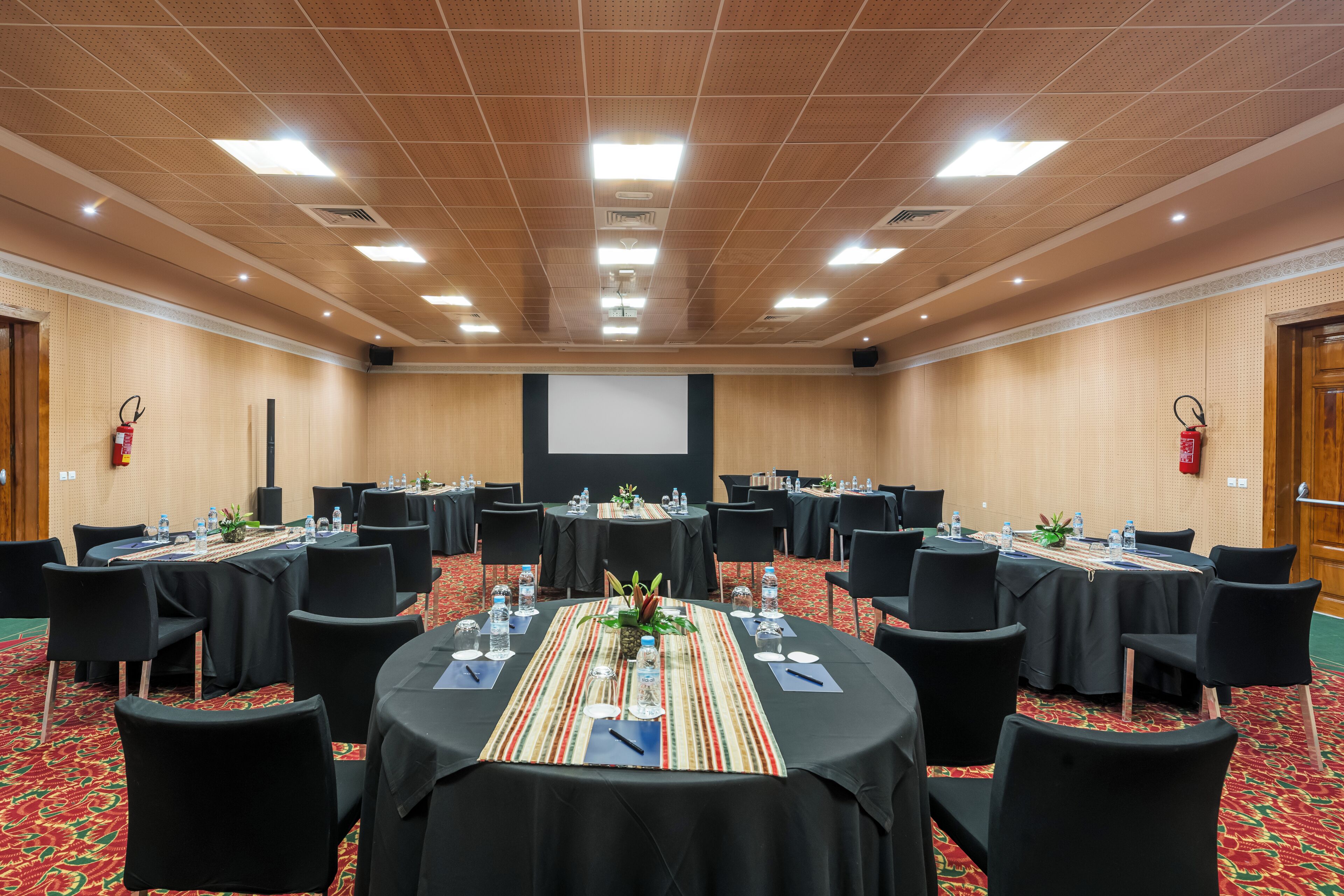 A conference room with round tables, black chairs, and a projector screen.