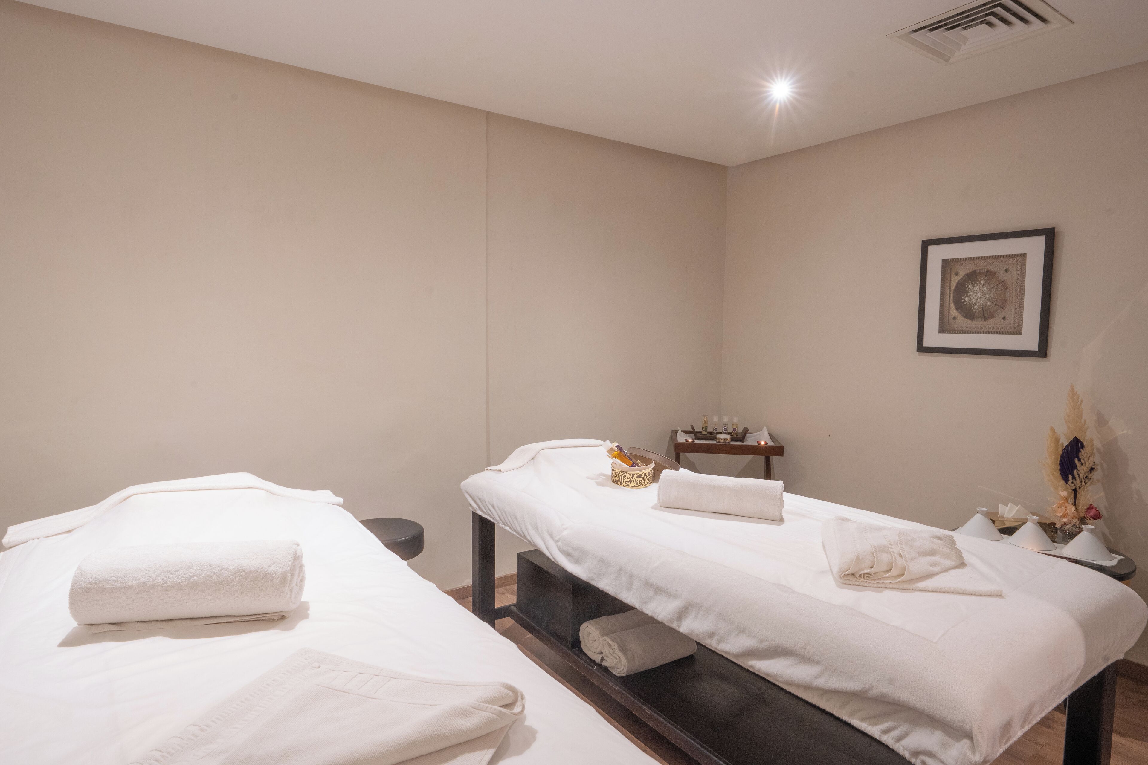 Ein Spa-Raum mit zwei Massagetischen, jeweils mit Handtuch und kleinem Tisch mit Kerzen und einem dekorativen Gegenstand.