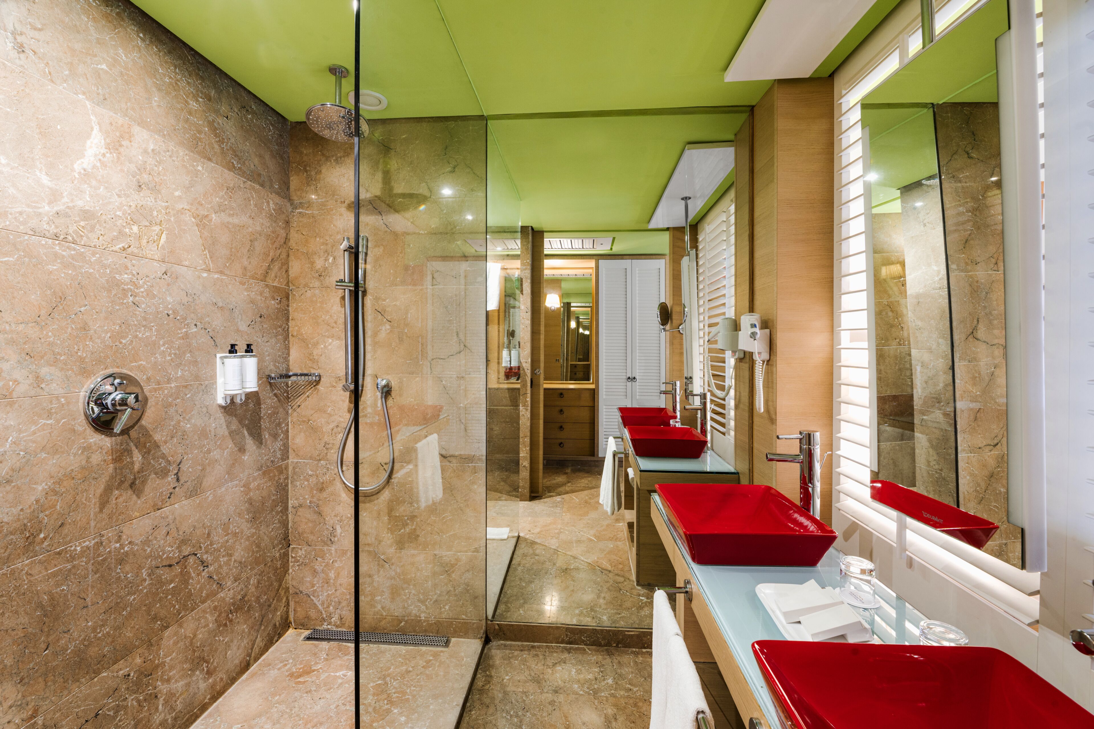Un baño moderno con ducha de vidrio, paredes de mármol y lavamanos rojos.