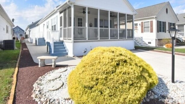 Een gelijkvloers huis met een overdekte veranda en een voortuin met een kleine struik en looppaden.