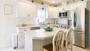 Een moderne keuken met witte kastjes, roestvrijstalen apparatuur en een centraal eiland met stoelen.