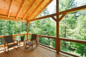 Une terrasse en bois avec deux fauteuils à bascule et une petite table, donnant sur une zone boisée.
