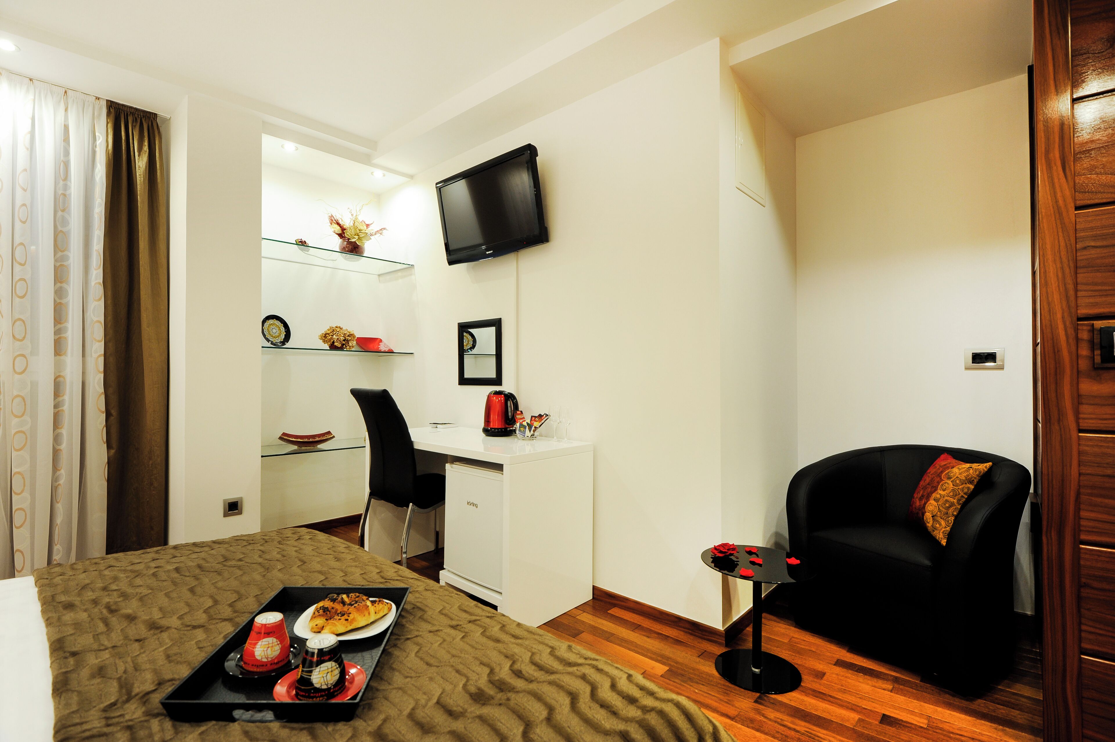 A compact hotel room with a bed, a desk, a TV, a sofa, and a tray with food.