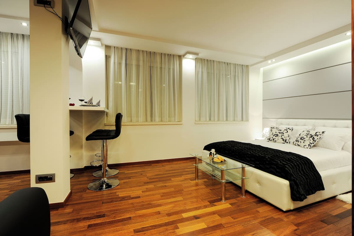 Una habitación de hotel moderna con una cama grande, una mesa de vidrio, una silla negra y un televisor fijado en la pared.