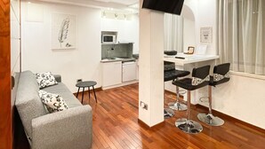 A modern living room with a grey sofa, a small round table, and a kitchen area with a microwave and sink.