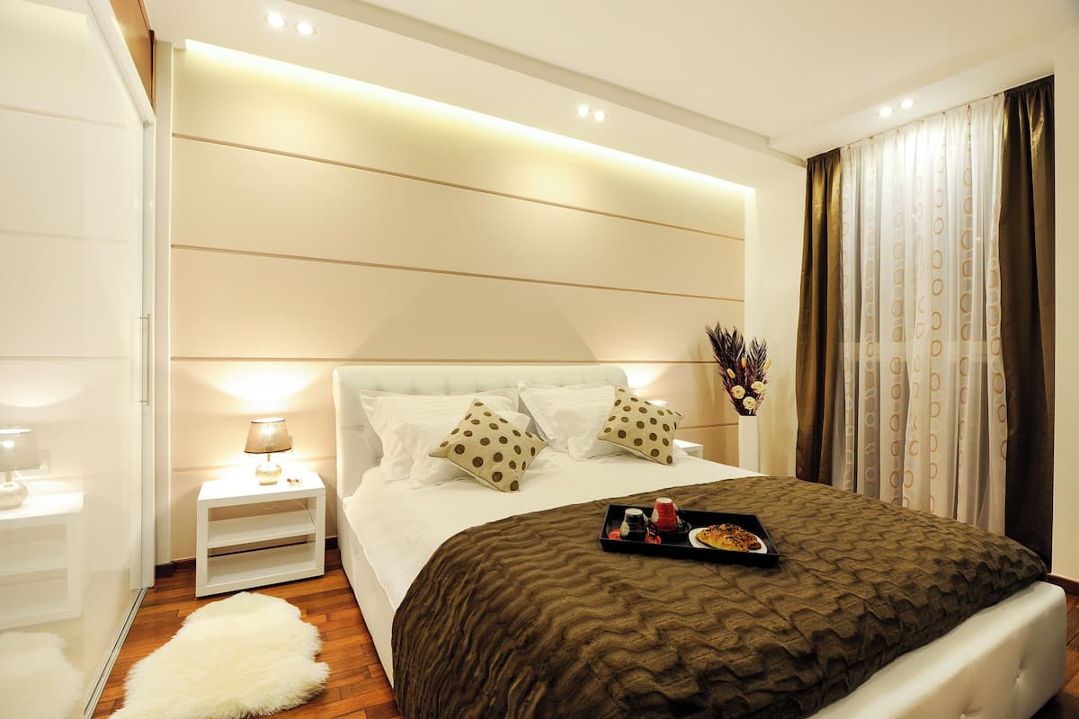 Habitación de hotel moderna con una cama bien hecha, una mesita de noche con lámpara y una bandeja con alimentos para el desayuno.