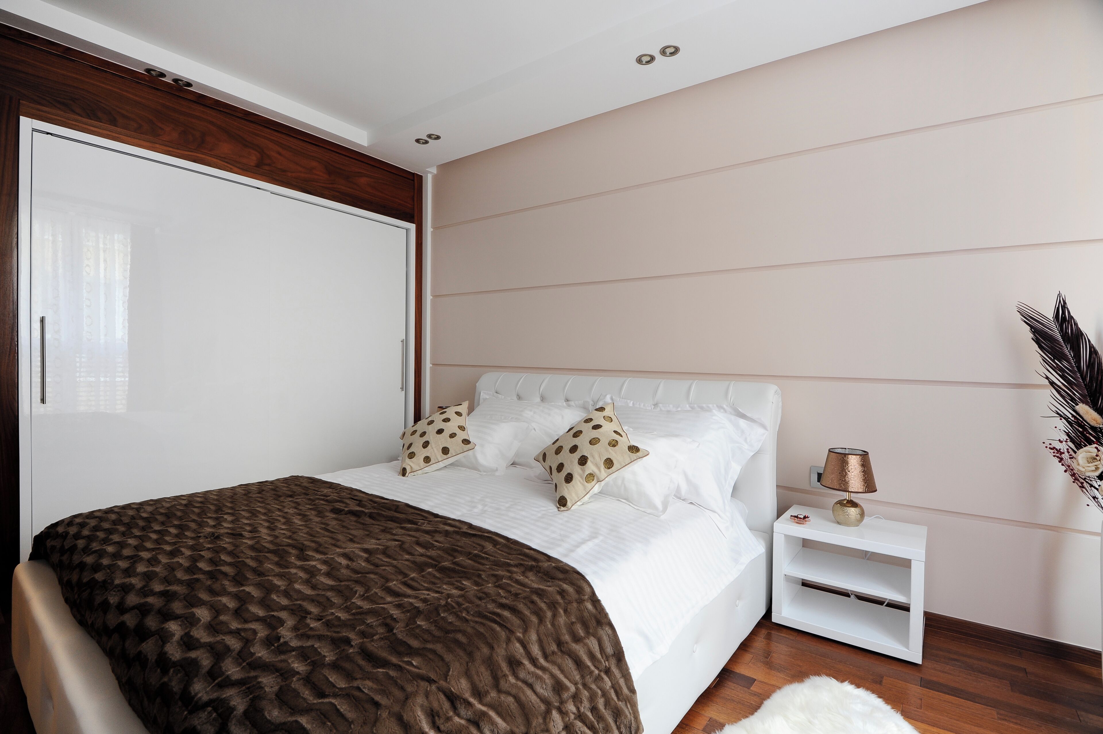 Un dormitorio con cama, mesita de noche blanca y estante en la pared.