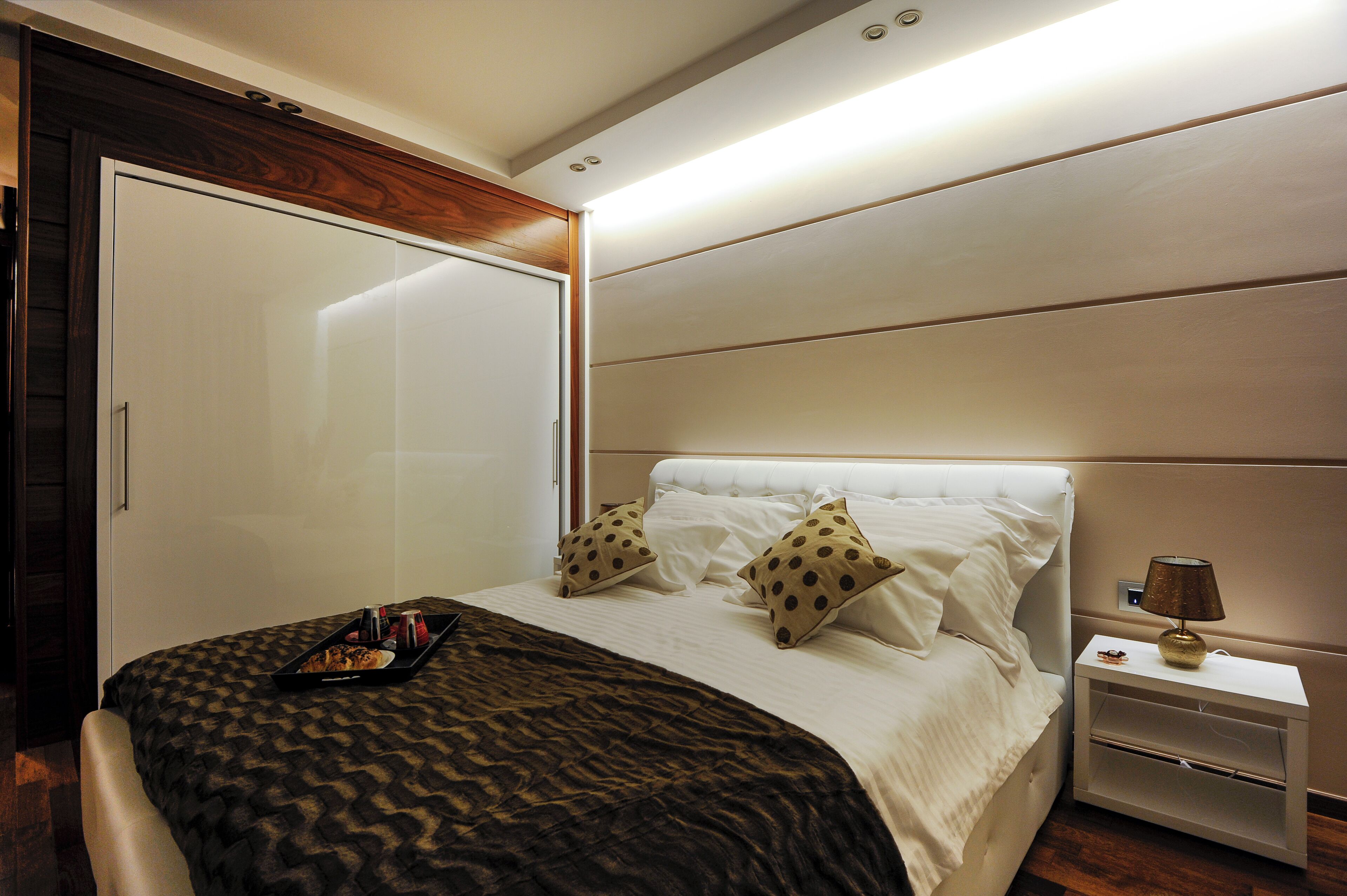 A neatly made bed with a patterned bedspread, two pillows, a tray with items, and a bedside table with a lamp.