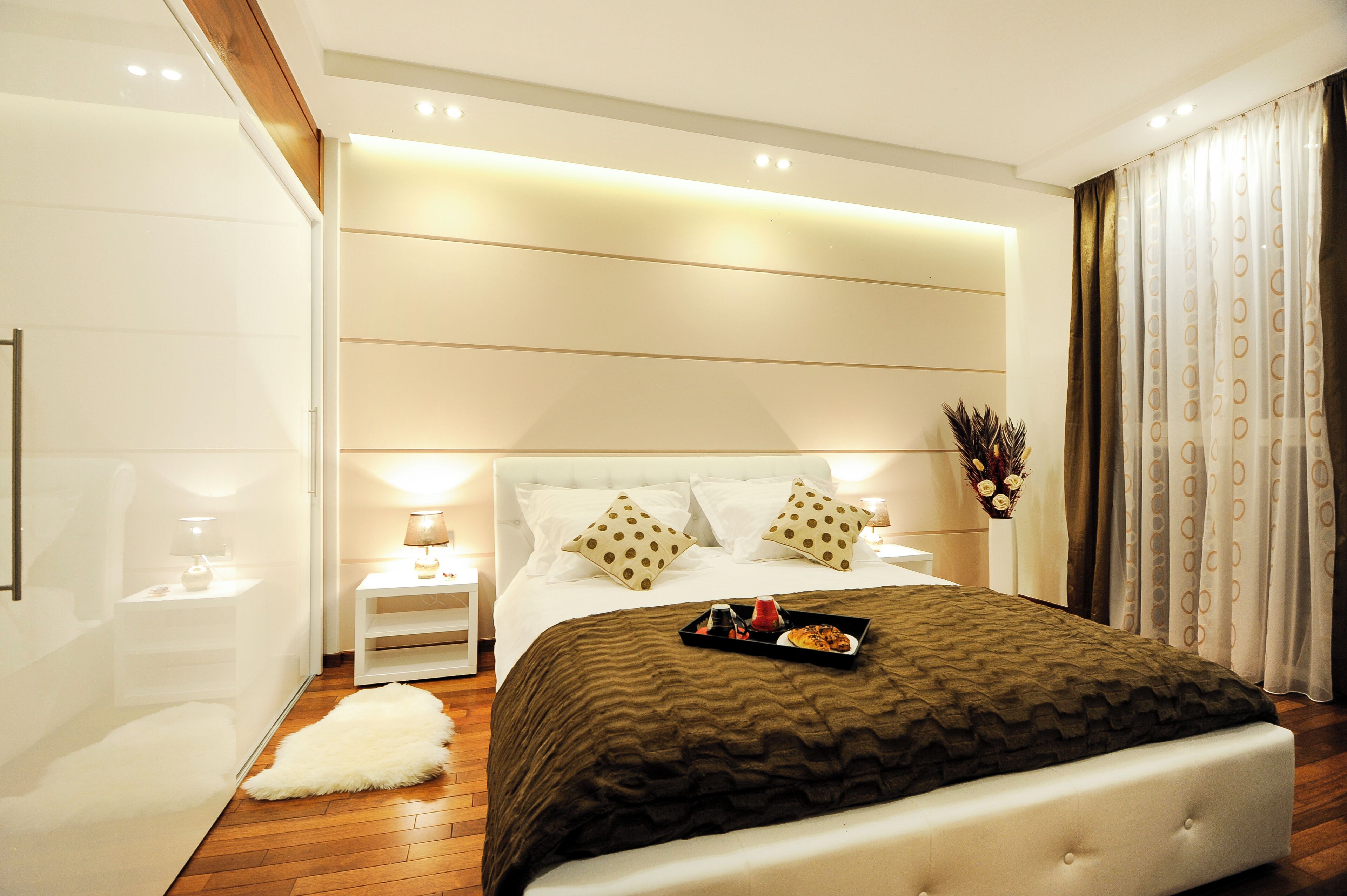 A modern bedroom with a large bed, bedside tables, a fluffy rug, and a nightstand with a lamp.