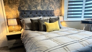 A bedroom with a tufted headboard, a grey bedspread, and a bedside lamp.