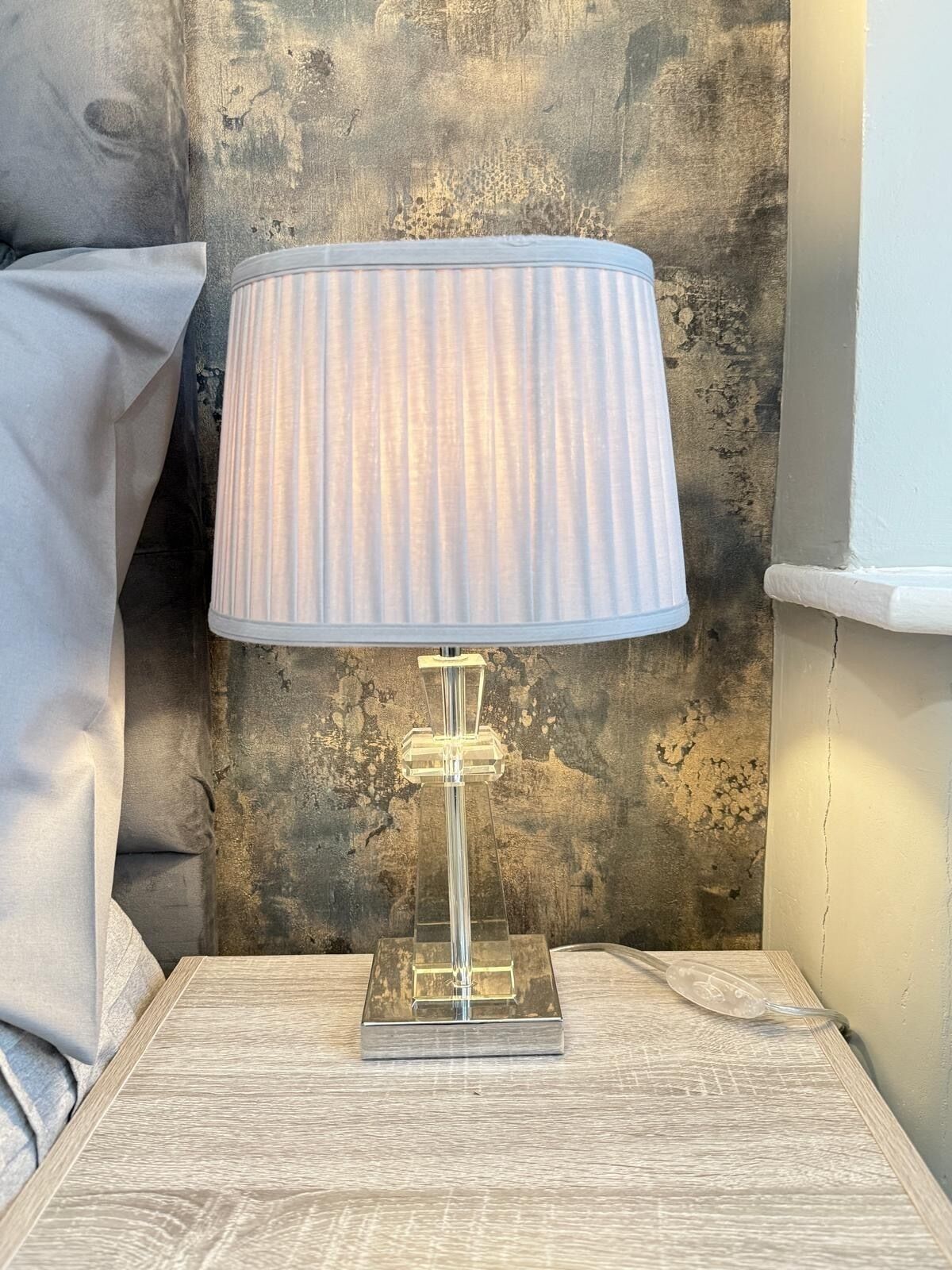 A clear glass table lamp with a ribbed lampshade on a textured wooden nightstand.