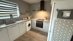 A modern kitchen with white cabinets, a built-in washing machine, an oven, and a refrigerator with a geometric tile pattern.