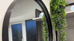 A bathroom with a round mirror, a window with frosted glass, and a potted plant on a shelf.