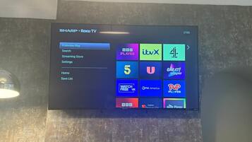 A Sharp Roku TV mounted on a textured wall with a menu interface.