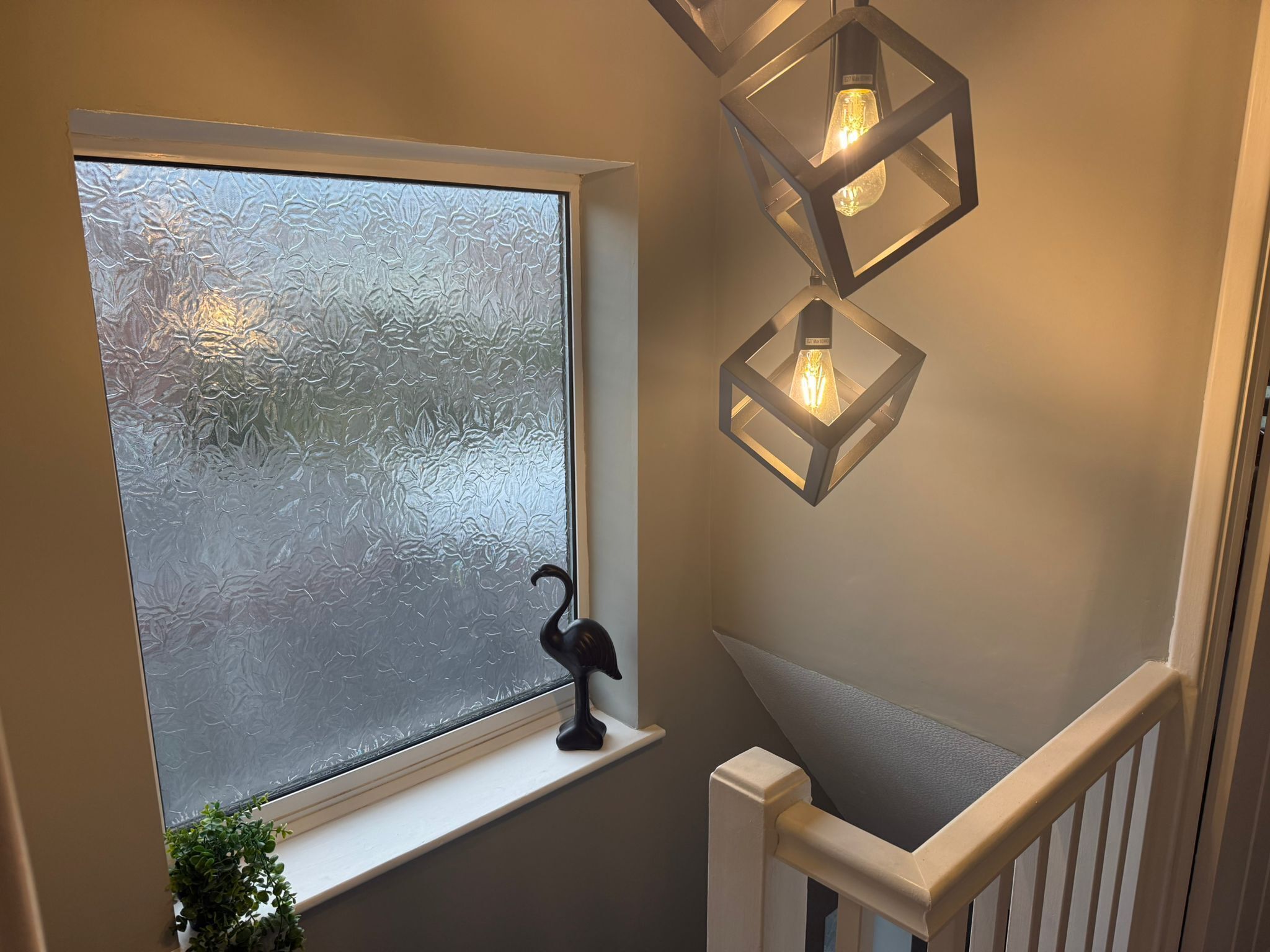 A staircase with a frosted glass window, a black bird decoration, and two hanging light fixtures.