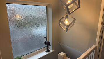 A staircase with a frosted glass window, a black bird decoration, and two hanging light fixtures.