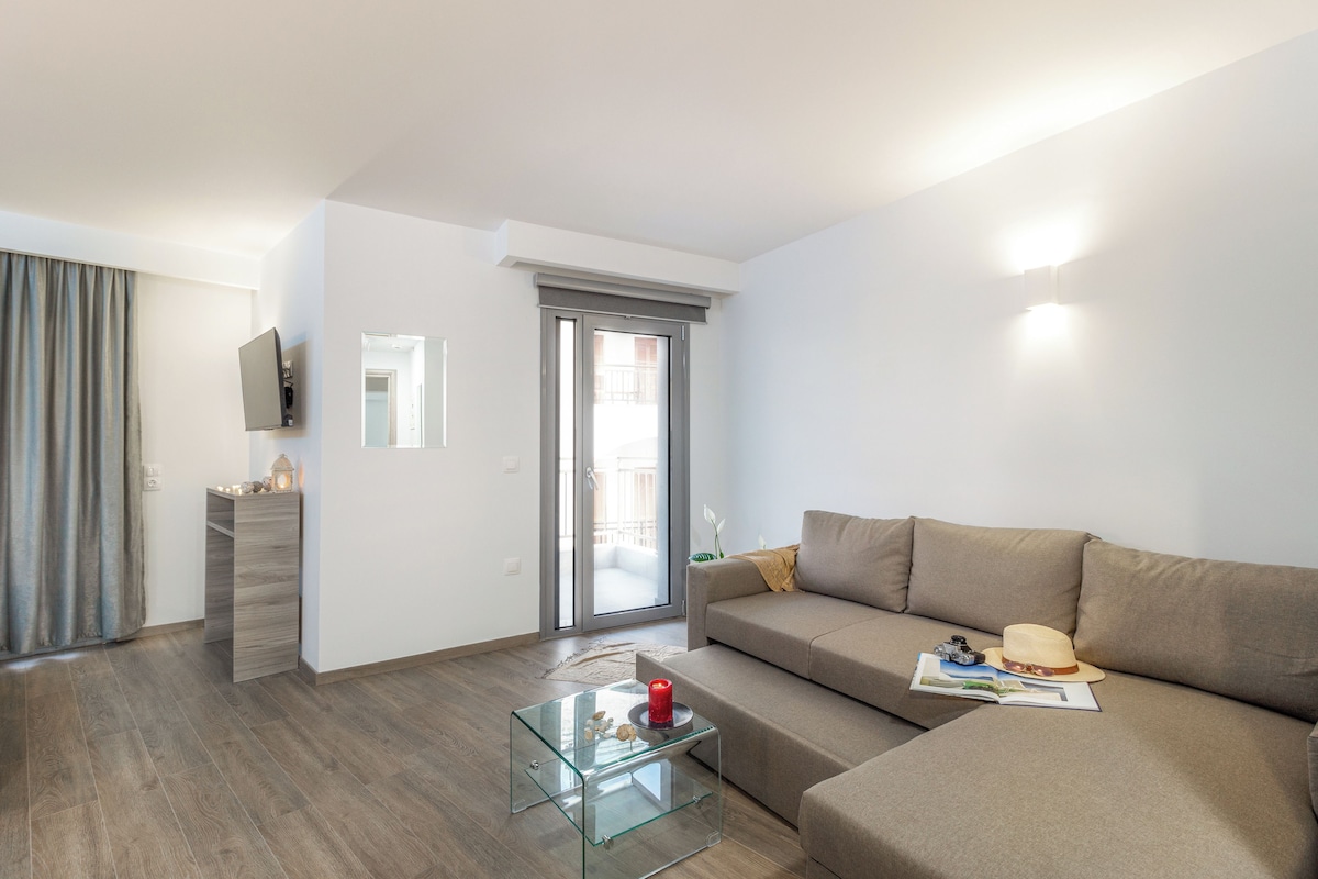 A modern living room with a glass coffee table, a beige sofa, and a flat-screen TV mounted on the wall.