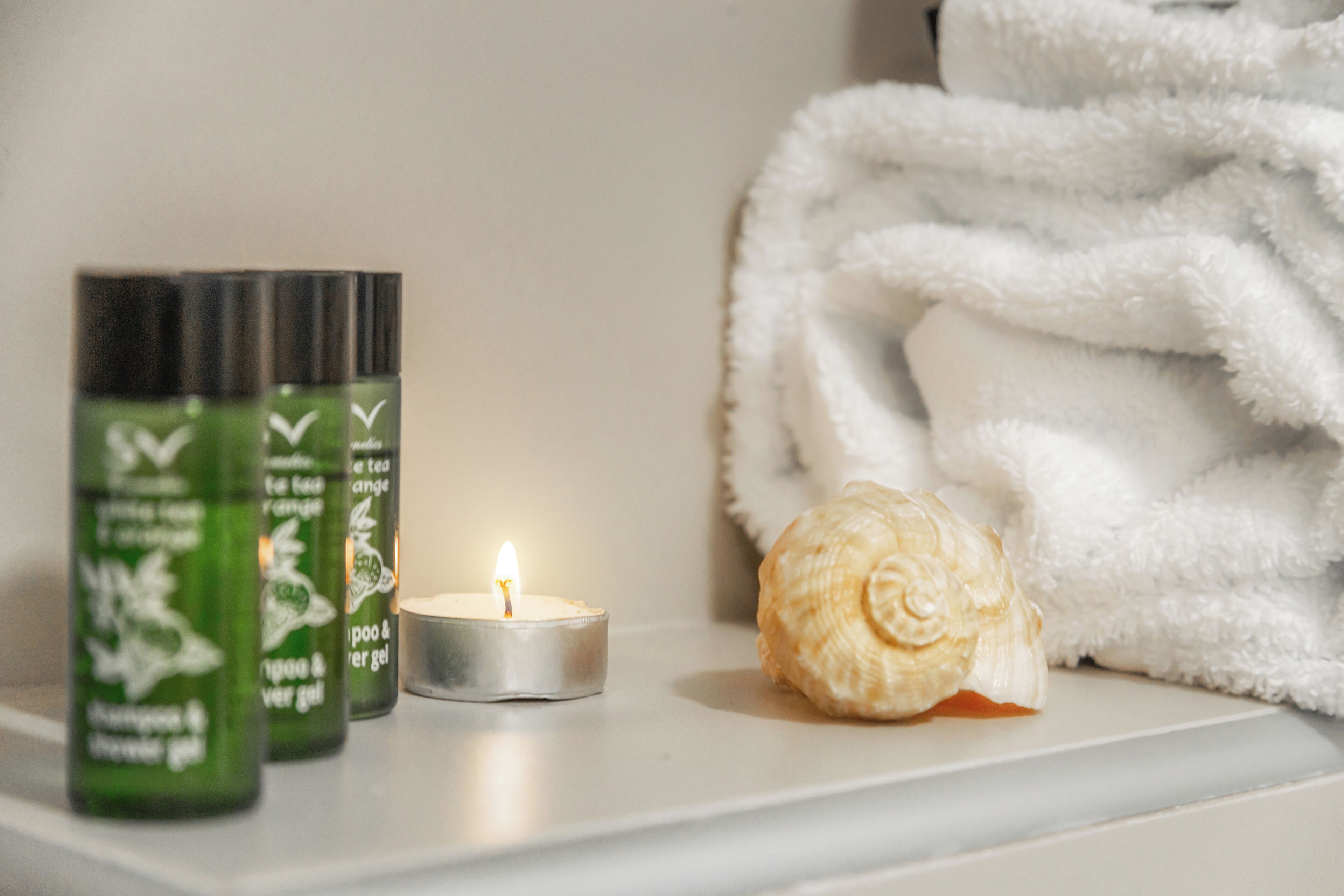 Une étagère avec trois bouteilles de shampoing et d’après-shampoing, une bougie allumée et un coquillage.