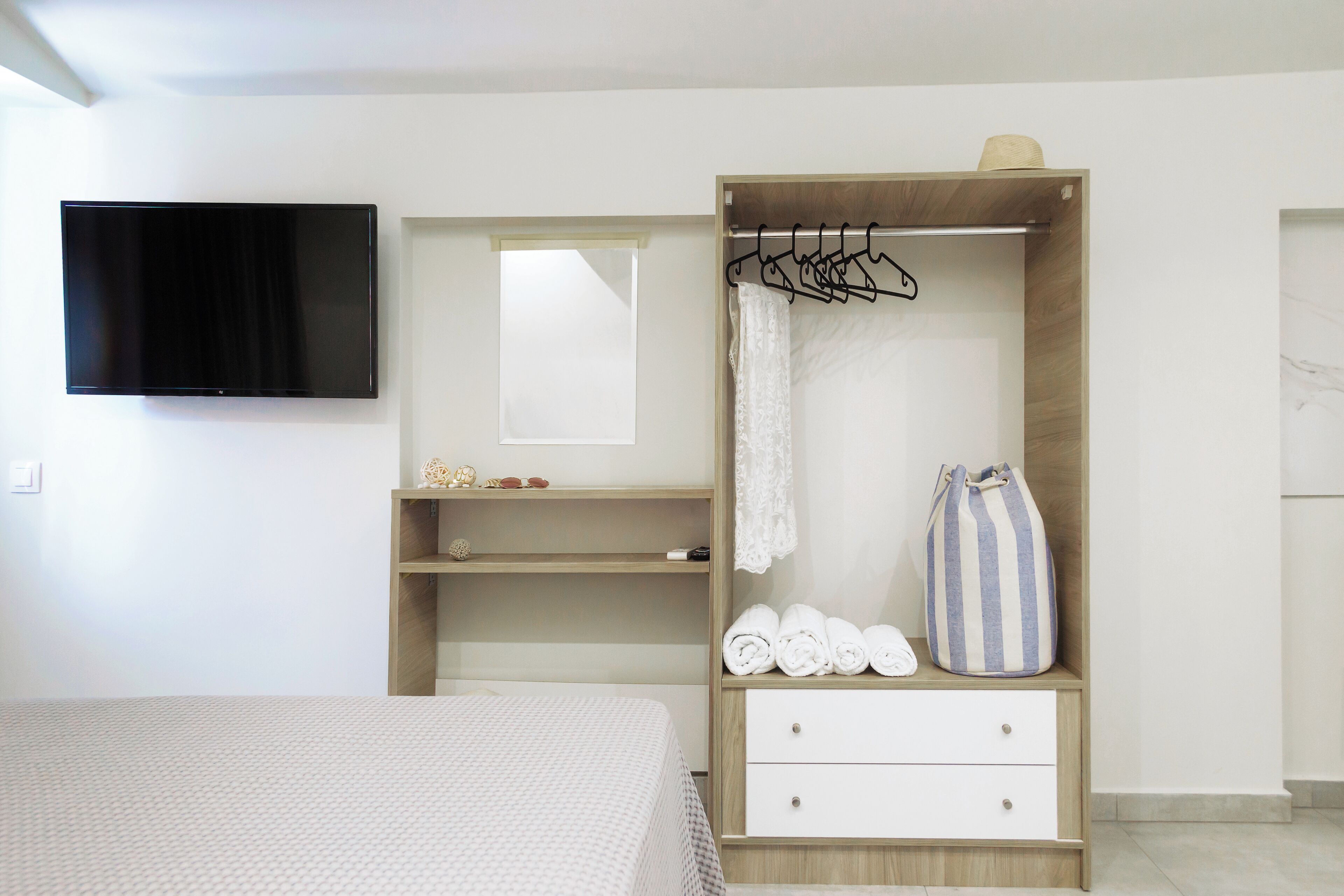 A bedroom with a bed, a wardrobe with hangers, a TV, and a window.