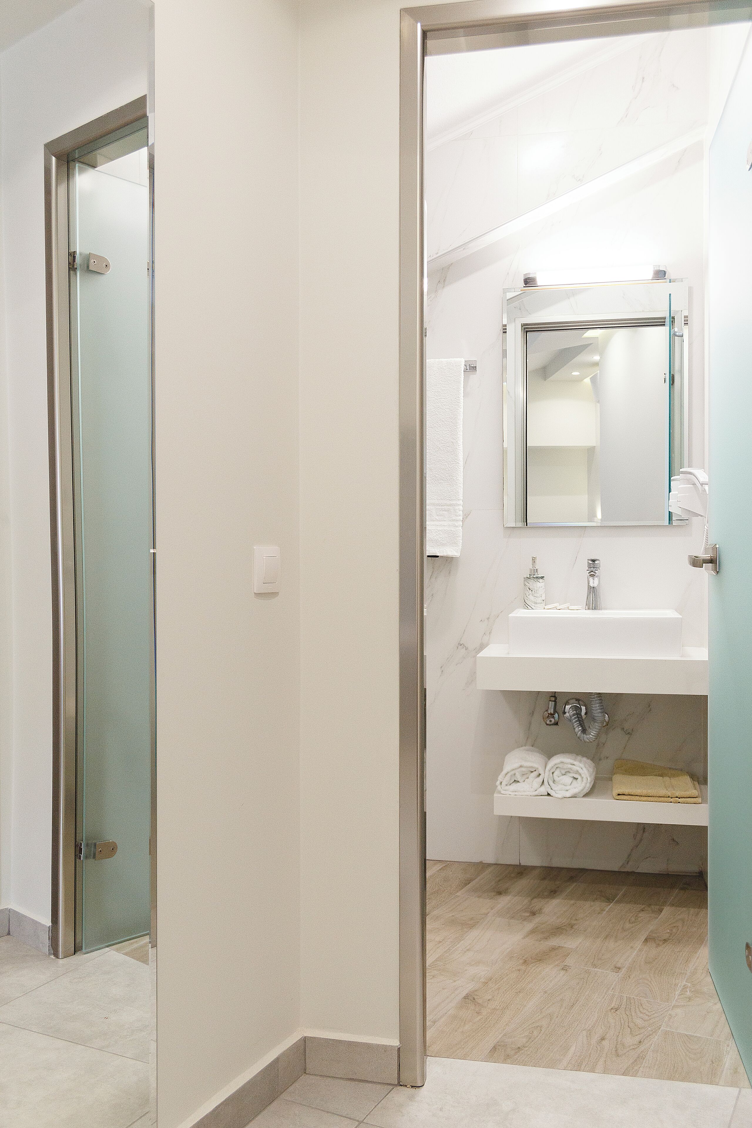 A modern bathroom with a glass door, a white sink, a mirror, and a towel rack.