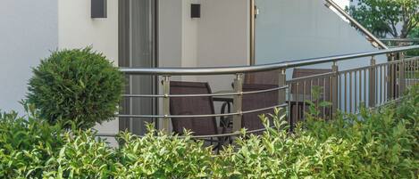 Ein Balkon mit Metallgeländer, einem kleinen Topfpflanzen und einem Stuhl.